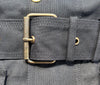 Close-up of a black waxed cotton jacket belt with a brass roller buckle and eyelets on a matching black garment.
