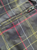 Close-up of a plaid jacket or coat fabric with a zippered pocket, featuring a dark gray base with red, yellow, and white windowpane lines.